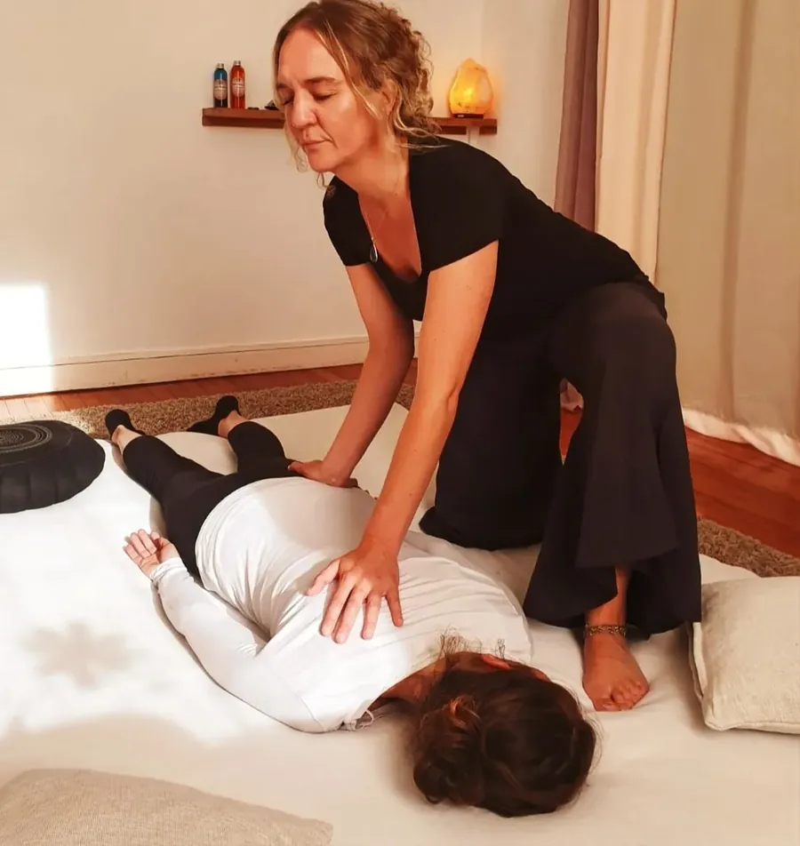 Claire, à genoux au sol, pose ses mains sur le dos d'une personne allongée sur un futon
