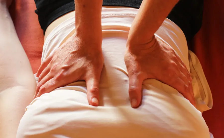 Deux mains pressent le bas du dos, à travers un drap
